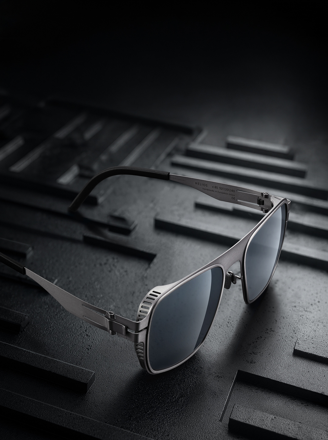 OVVO Optics Ti2 Helios titanium sunglasses on a dark precision-engineered surface